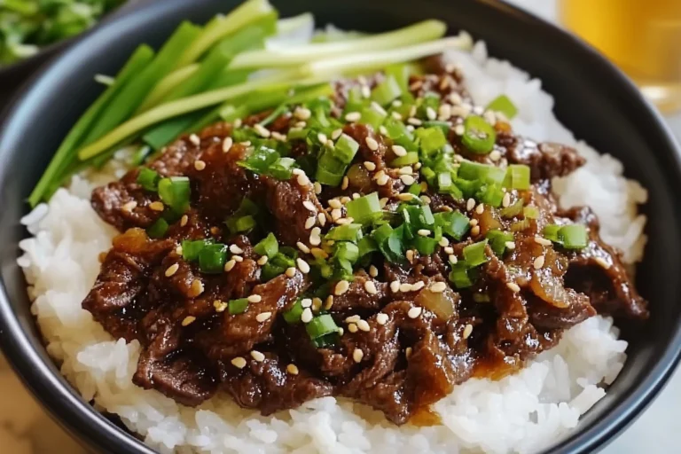 Korean beef bowl served over white rice, topped with sesame seeds and green onions.